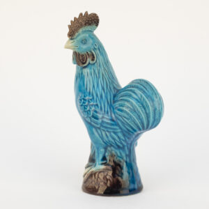 Coq décoratif en céramique émaillée bleu turquoise sur base brune, vu de trois quarts.