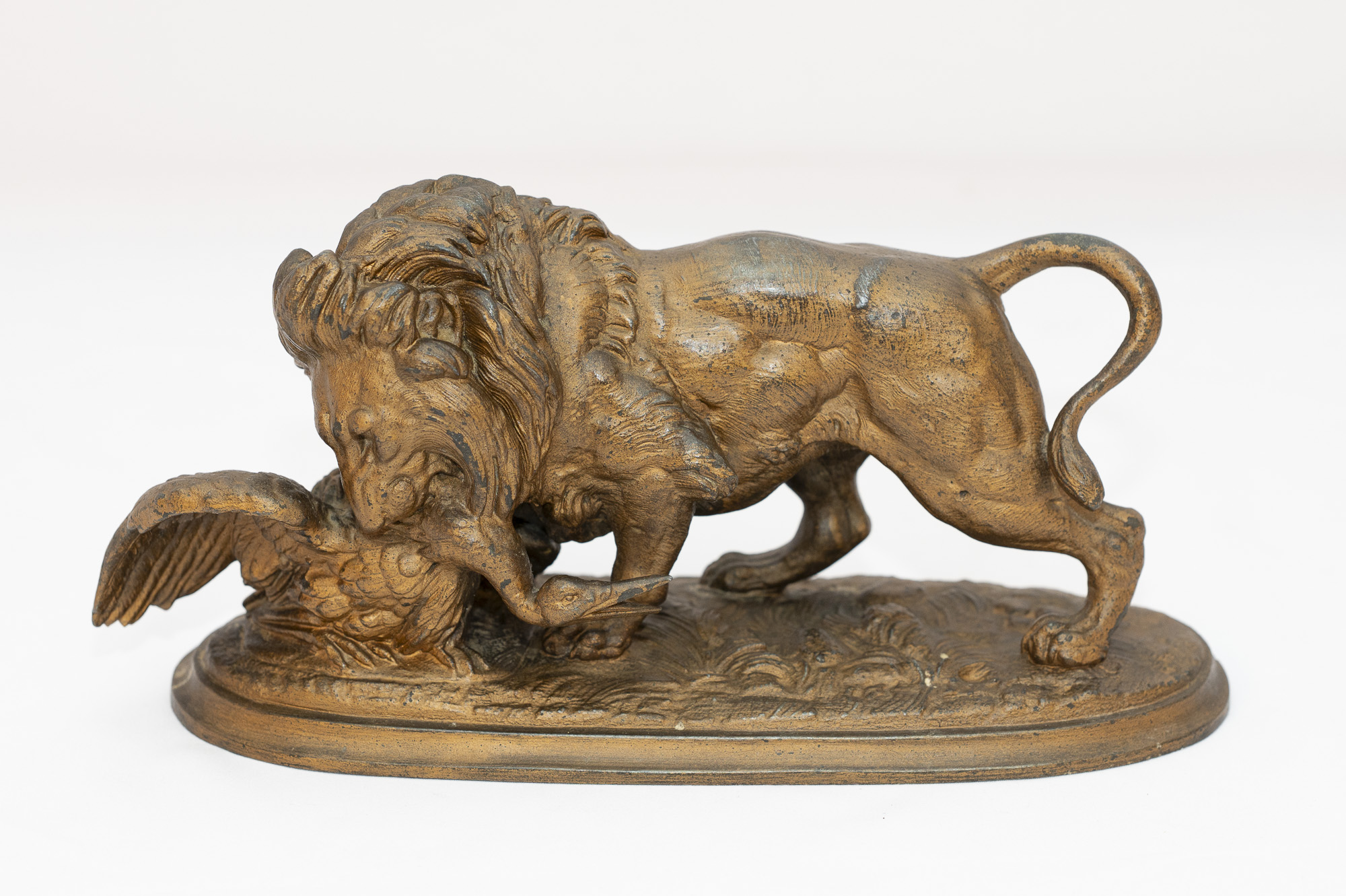 Sculpture en bronze montrant un lion maintenant un oiseau sous ses pattes, sur une base ovale texturée.