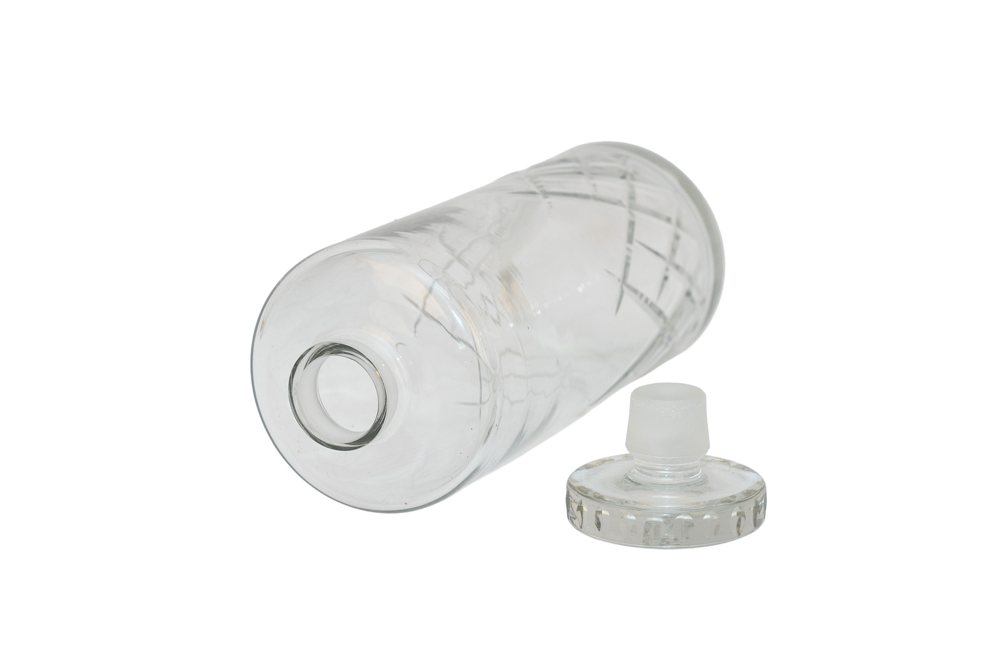 Carafe en cristal couchée avec l’ouverture du col au premier plan et le bouchon facetté posé à côté.